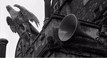 Movie still from “Night of the Eagle” (1962), directed by Sidney Hayers – An old building has a bird perched on top of it; Wide shot, Low angle