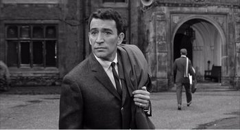 Movie still from “Night of the Eagle” (1962), directed by Sidney Hayers – A black and white photo of a man in a suit and tie; Medium shot, Low angle