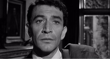 Movie still from “Night of the Eagle” (1962), directed by Sidney Hayers – Black and white photograph of a man in a suit and tie; Close Up shot, Low angle