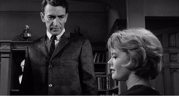 Movie still from “Night of the Eagle” (1962), directed by Sidney Hayers – A man and a woman standing next to each other in a room; Medium shot, Over the shoulder angle