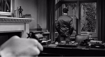 Movie still from “Night of the Eagle” (1962), directed by Sidney Hayers – A black and white photo of a man in a suit looking out a window; Medium shot, Over the shoulder angle