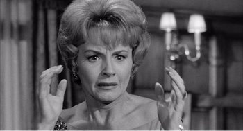 Movie still from “Night of the Eagle” (1962), directed by Sidney Hayers – An older woman with her hands up in the air; Close Up shot, Over the shoulder angle