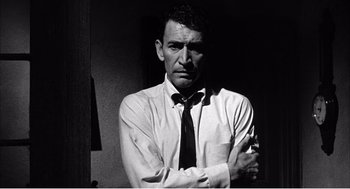 Movie still from “Night of the Eagle” (1962), directed by Sidney Hayers – A black and white photo of a man with his arms crossed; Medium shot, Low angle