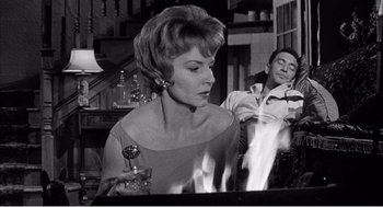 Movie still from “Night of the Eagle” (1962), directed by Sidney Hayers – An old photo of a woman and a man smoking a cigarette; Medium shot, Low angle
