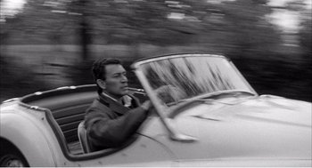 Movie still from “Night of the Eagle” (1962), directed by Sidney Hayers – A black and white photo of a man driving a car; Medium shot, High angle