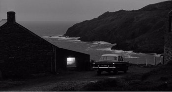 Movie still from “Night of the Eagle” (1962), directed by Sidney Hayers – A car parked on the side of the road near the ocean; Extreme Wide shot, High angle