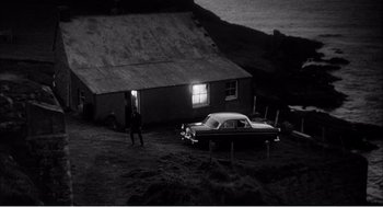 Movie still from “Night of the Eagle” (1962), directed by Sidney Hayers – An old car parked in front of a house at night; Extreme Wide shot, High angle