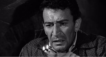 Movie still from “Night of the Eagle” (1962), directed by Sidney Hayers – A black and white photo of a man lighting a cigarette; Close Up shot, Low angle