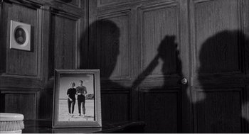 Movie still from “Night of the Eagle” (1962), directed by Sidney Hayers – A shadow of a man and a woman standing next to each other in front of a picture frame; Medium shot, Overhead angle