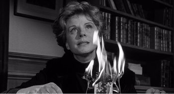 Movie still from “Night of the Eagle” (1962), directed by Sidney Hayers – An older woman is looking at a candle on fire; Close Up shot, Low angle