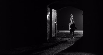 Movie still from “Night of the Eagle” (1962), directed by Sidney Hayers – A person walking in the dark near a brick wall; Wide shot, Low angle