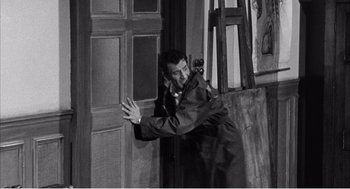 Movie still from “Night of the Eagle” (1962), directed by Sidney Hayers – A black and white photo of a man hugging another man in front of an easel; Medium shot, High angle