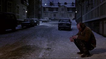 Movie still from “Night on Earth” (1991), directed by Jim Jarmusch – A man sitting on the side of a road in the snow; Wide shot, High angle