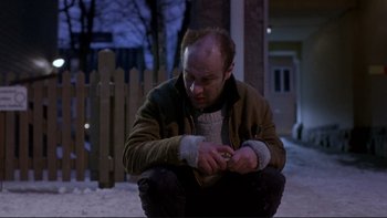 Movie still from “Night on Earth” (1991), directed by Jim Jarmusch – A man sitting on the ground looking at his cell phone; Medium shot, Low angle