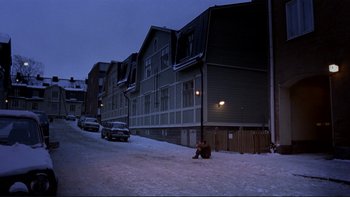 Movie still from “Night on Earth” (1991), directed by Jim Jarmusch – A person sitting on the side of a road near a building; Extreme Wide shot, High angle