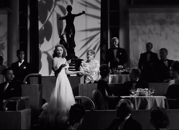 Movie still from “Nightmare Alley” (1947), directed by Edmund Goulding – A woman in a white dress standing in front of a man in a suit; Wide shot, Low angle