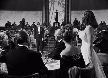 Movie still from “Nightmare Alley” (1947), directed by Edmund Goulding – A black and white photo of people sitting at a table; Medium shot, Over the shoulder angle