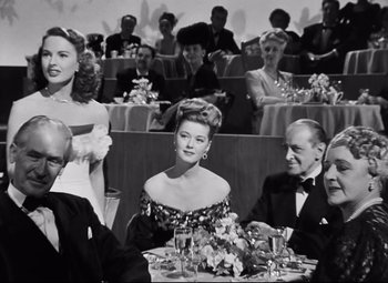Movie still from “Nightmare Alley” (1947), directed by Edmund Goulding – A black and white photo of people sitting at a table; Medium shot, Over the shoulder angle