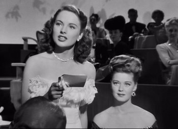 Movie still from “Nightmare Alley” (1947), directed by Edmund Goulding – Two women in a movie theater , one of which is holding a book; Medium shot, Low angle
