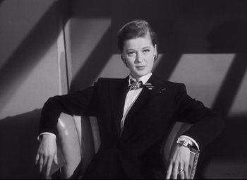 Movie still from “Nightmare Alley” (1947), directed by Edmund Goulding – A woman in a suit sitting in a chair; Medium shot, Low angle