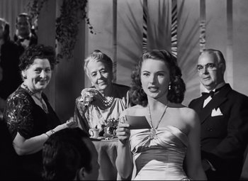 Movie still from “Nightmare Alley” (1947), directed by Edmund Goulding – A woman holding a tray of food in front of a group of people; Medium shot, Over the shoulder angle