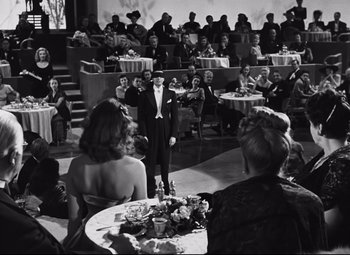 Movie still from “Nightmare Alley” (1947), directed by Edmund Goulding – A man standing in front of an audience at a formal event; Wide shot, High angle