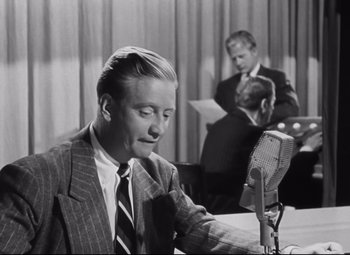 Movie still from “Nightmare Alley” (1947), directed by Edmund Goulding – A black and white photo of a man in a suit and tie; Medium shot, Over the shoulder angle
