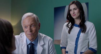 Movie still from “Nightmare Cinema” (2018), directed by Alejandro Brugués – A man and a woman in lab coats in front of a picture; Close Up shot, Over the shoulder angle