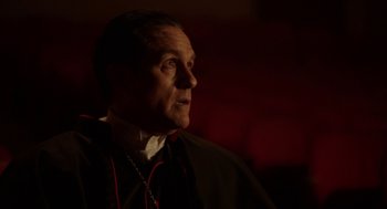 Movie still from “Nightmare Cinema” (2018), directed by Alejandro Brugués – A man wearing a priest's outfit looking to his left; Close Up shot, Over the shoulder angle