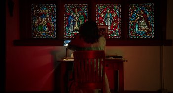 Movie still from “Nightmare Cinema” (2018), directed by Alejandro Brugués – A woman sitting in front of a computer in front of stained glass windows; Wide shot, Low angle