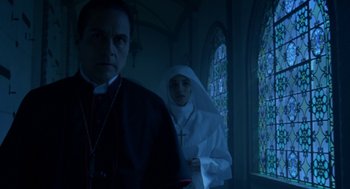 Movie still from “Nightmare Cinema” (2018), directed by Alejandro Brugués – A priest and a nun in a dark room; Medium shot, Low angle