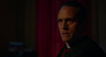 Movie still from “Nightmare Cinema” (2018), directed by Alejandro Brugués – A man wearing a priest's outfit looking at the camera; Close Up shot, Over the shoulder angle