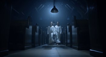 Movie still from “Nightmare Cinema” (2018), directed by Alejandro Brugués – Two men in white robes are standing in a dark room; Wide shot, Low angle