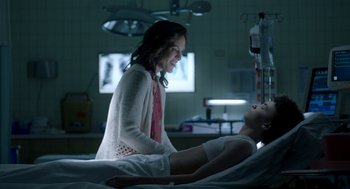 Movie still from “Nightmare Cinema” (2018), directed by Alejandro Brugués – A woman standing next to a man laying in a hospital bed; Medium shot, Over the shoulder angle