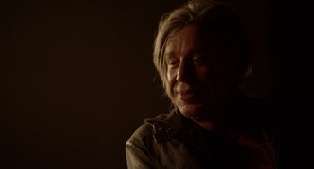 Movie still from “Nightmare Cinema” (2018), directed by Alejandro Brugués – A man with long blonde hair is sitting in a dark room; Close Up shot, Over the shoulder angle
