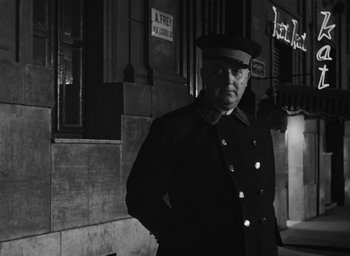 Movie still from “Nights of Cabiria” (1957), directed by Federico Fellini – A man in a uniform standing in front of a building; Medium shot, Low angle