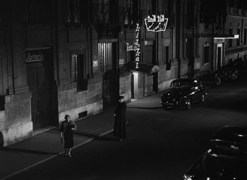 Movie still from “Nights of Cabiria” (1957), directed by Federico Fellini – A woman standing on the side of the street at night; Extreme Wide shot, High angle