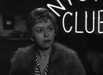Movie still from “Nights of Cabiria” (1957), directed by Federico Fellini – A black - and - white photo of a woman in front of a neon sign; Close Up shot, Low angle