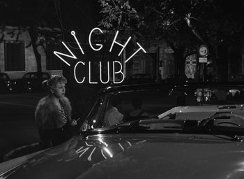 Movie still from “Nights of Cabiria” (1957), directed by Federico Fellini – A black and white photo of a woman in a car at night; Wide shot, Low angle