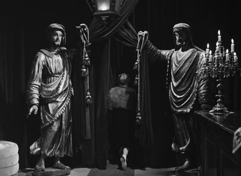 Movie still from “Nights of Cabiria” (1957), directed by Federico Fellini – A man standing in front of two statues; Wide shot, Low angle