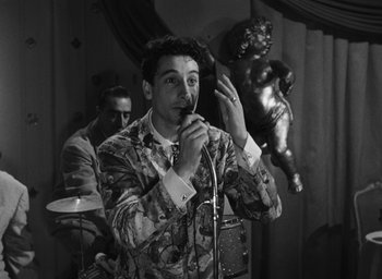 Movie still from “Nights of Cabiria” (1957), directed by Federico Fellini – A man is singing into a microphone while another man watches; Medium shot, Low angle