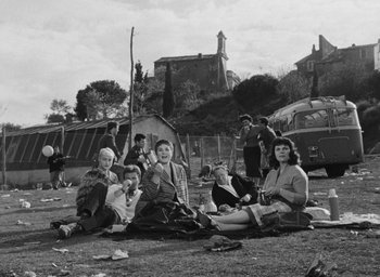 Movie still from “Nights of Cabiria” (1957), directed by Federico Fellini – A black and white photo of a group of people sitting on the ground; Wide shot, High angle