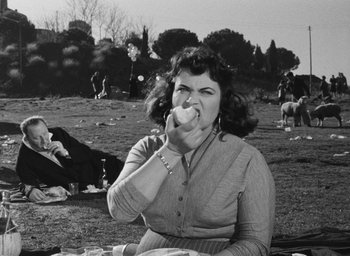 Movie still from “Nights of Cabiria” (1957), directed by Federico Fellini – An old photo of a woman sitting in the grass eating a sandwich; Medium shot, High angle