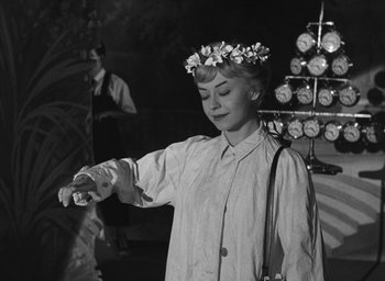 Movie still from “Nights of Cabiria” (1957), directed by Federico Fellini – A black and white photo of a woman wearing a flower crown; Medium shot, Over the shoulder angle
