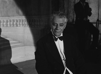 Movie still from “Nights of Cabiria” (1957), directed by Federico Fellini – An older man in a suit and bow tie in front of a building; Medium shot, Low angle