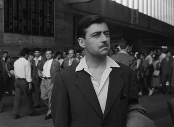 Movie still from “Nights of Cabiria” (1957), directed by Federico Fellini – Black and white photograph of a man in a crowd of people; Medium shot, Low angle