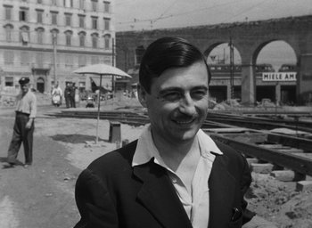 Movie still from “Nights of Cabiria” (1957), directed by Federico Fellini – A man in a suit standing in front of a train station; Close Up shot, Low angle