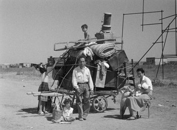 Movie still from “Nights of Cabiria” (1957), directed by Federico Fellini – An old black and white photo of a man and a woman and two children sitting in front of a wagon; Wide shot, High angle