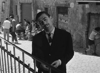Movie still from “Nights of Cabiria” (1957), directed by Federico Fellini – A black and white photo of a man smoking a cigarette; Medium shot, Low angle