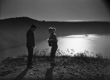 Movie still from “Nights of Cabiria” (1957), directed by Federico Fellini – A man and a woman standing next to a body of water; Wide shot, High angle